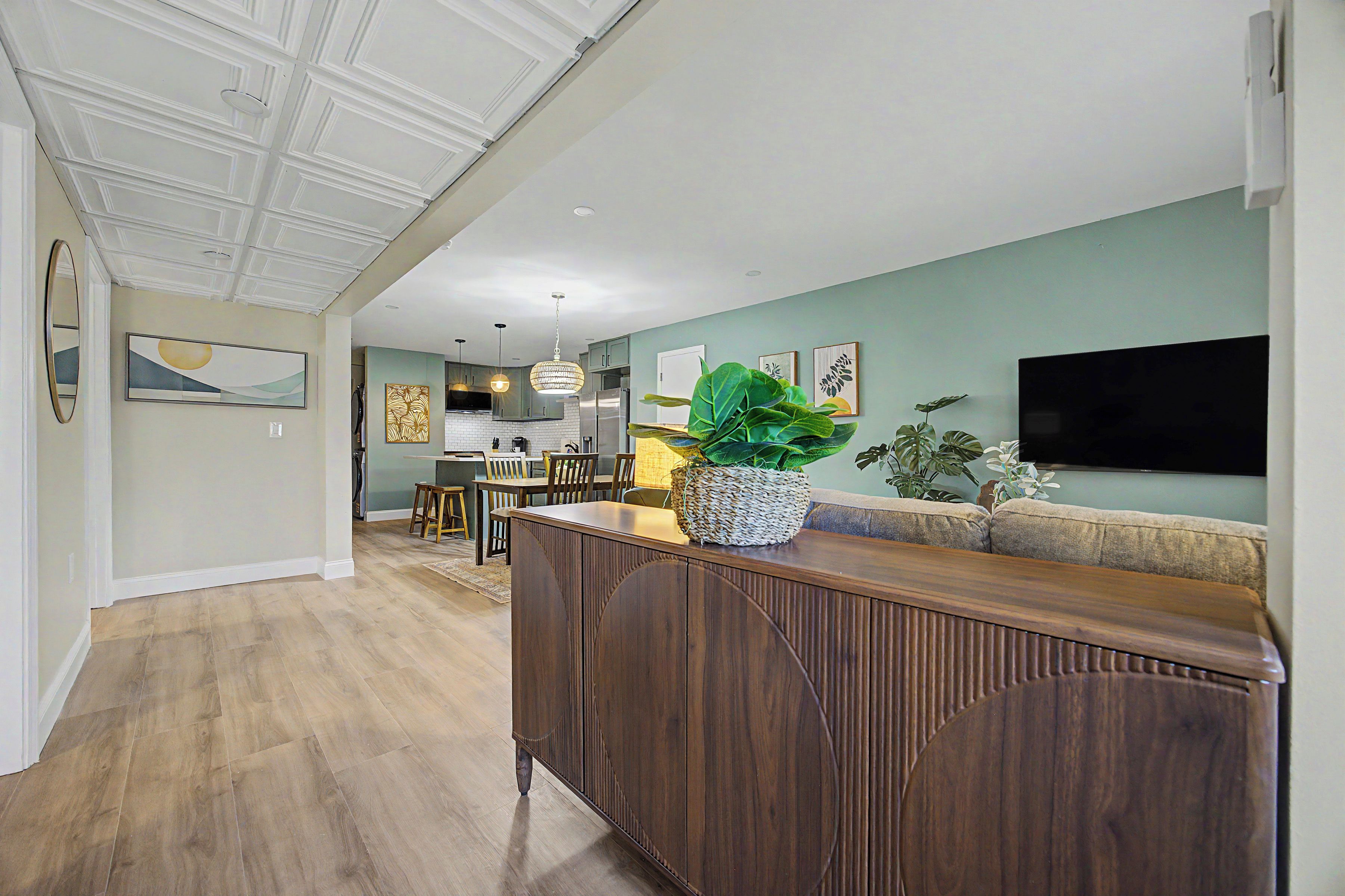 Un salon moderne avec un meuble de rangement en bois pour l’équipement audiovisuel, un téléviseur à écran plat et un coin repas avec une cuisine en arrière-plan.