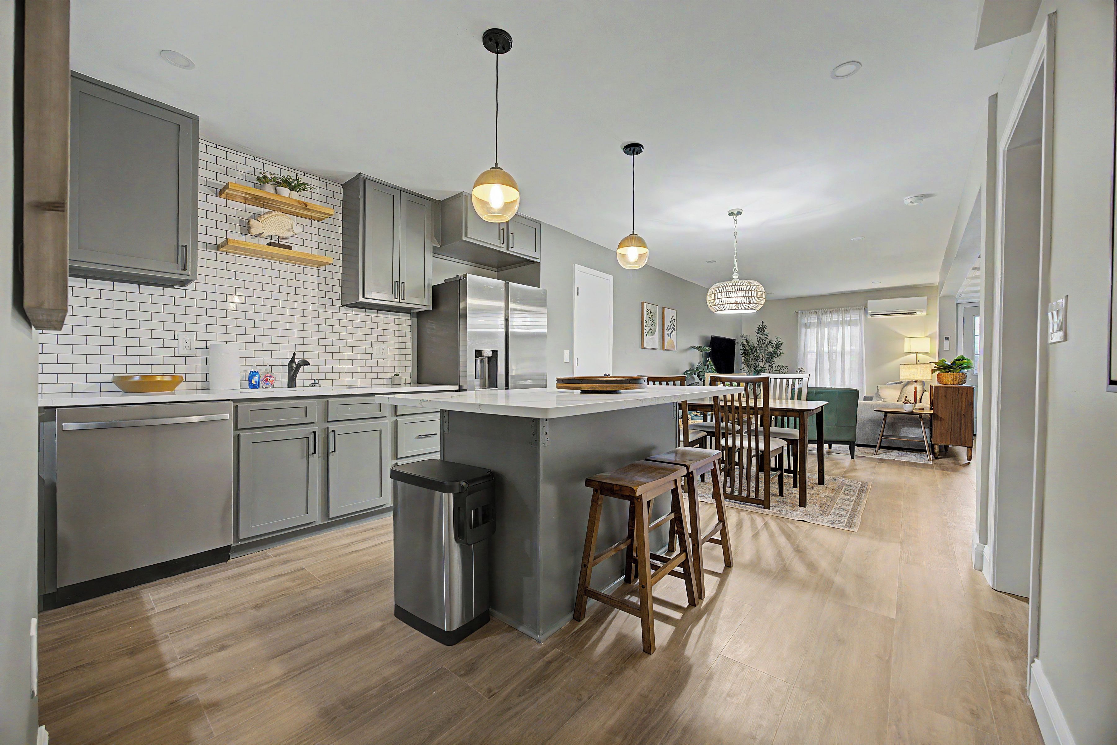 A modern kitchen with grey cabinets, a stainless steel refrigerator, and a central island with stools.