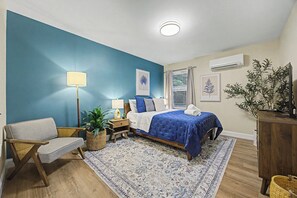 A bedroom with a bed, bedside tables, a chair, a floor lamp, and a large window with curtains.