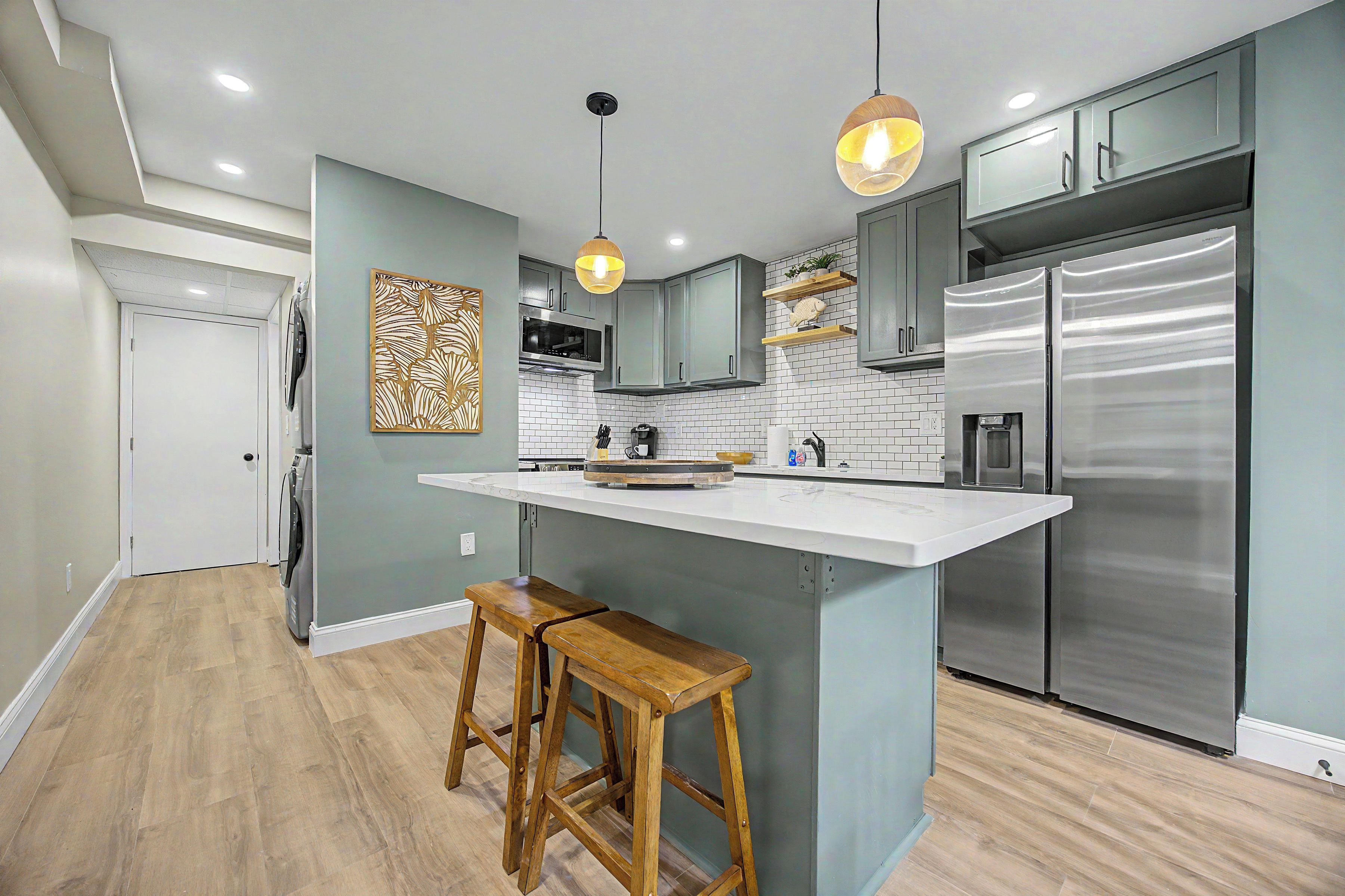 A modern kitchen with a central island, stainless steel appliances, and wooden bar stools.