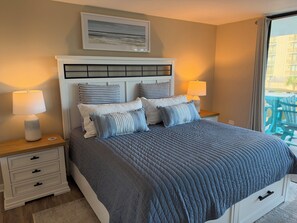 A bedroom with a large bed, two bedside tables with lamps, a headboard, and a painting above the bed. - Relaxing Oceanview Beach Retreat in Ocean Creek (Myrtle Beach)