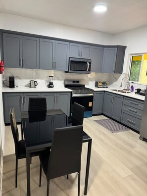 Een moderne keuken met grijze kastjes, een zwarte eettafel en een magnetron.