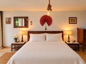 A hotel room with a large bed, two bedside tables with lamps, a mirror, and wall decorations including a fan and framed pictures. - Spacious loft at the foot of Pedra da Gávea.  Gated community with 24-hour security. (Rio de Janeiro)