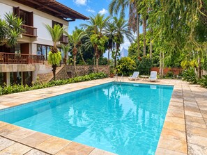 A swimming pool with tiled edges, surrounded by palm trees and a stone wall. - Spacious loft at the foot of Pedra da Gávea.  Gated community with 24-hour security. (Rio de Janeiro)