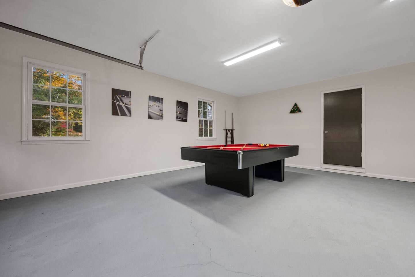 Una habitación con mesa de billar, ventana con vista a árboles y una puerta.