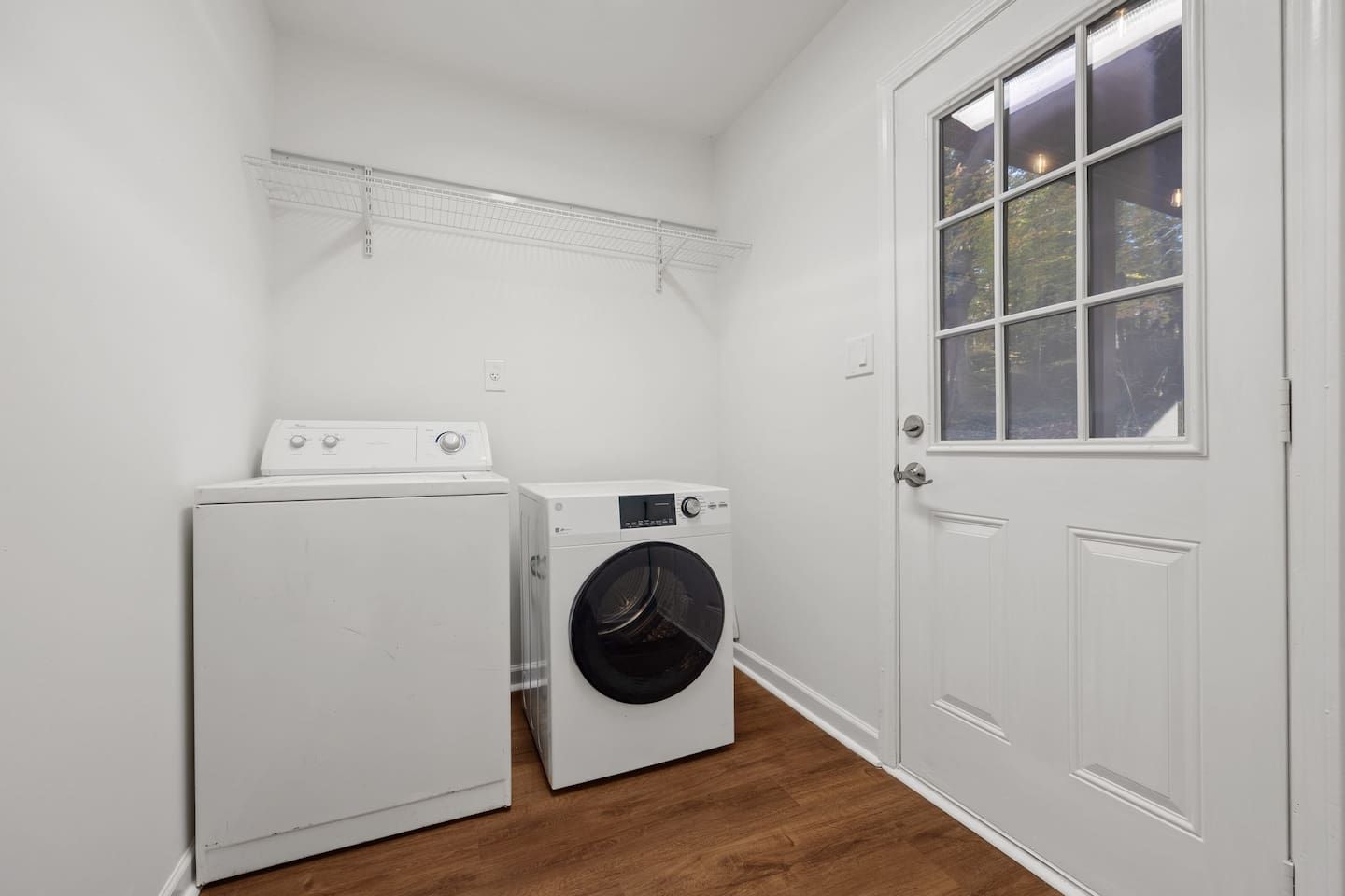 A laundry room with a white wall, a door, and a window.
