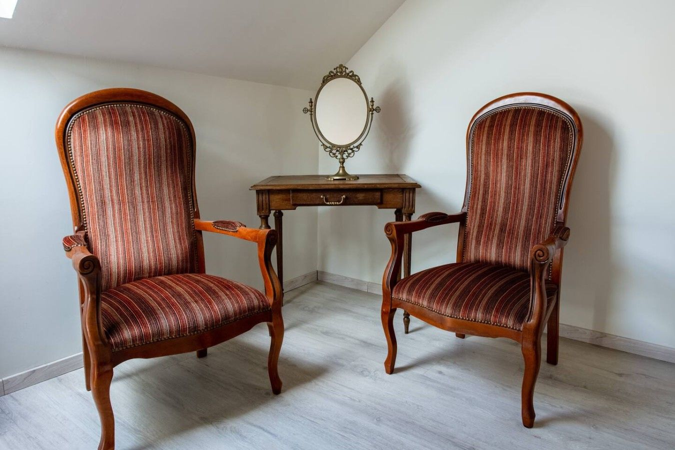 Deux fauteuils rembourrés avec des structures en bois, et une petite table avec un miroir placé entre les deux.