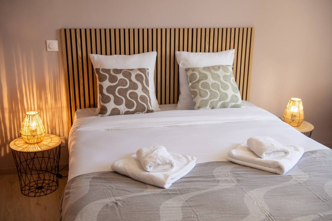 A hotel room with a bed, two pillows, two bedside lamps, and two towels on the bed.