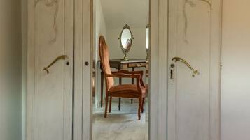 Ein Zimmer mit großem Kleiderschrank, Spiegel, Holzstuhl und Bett mit gemustertem Überwurf.