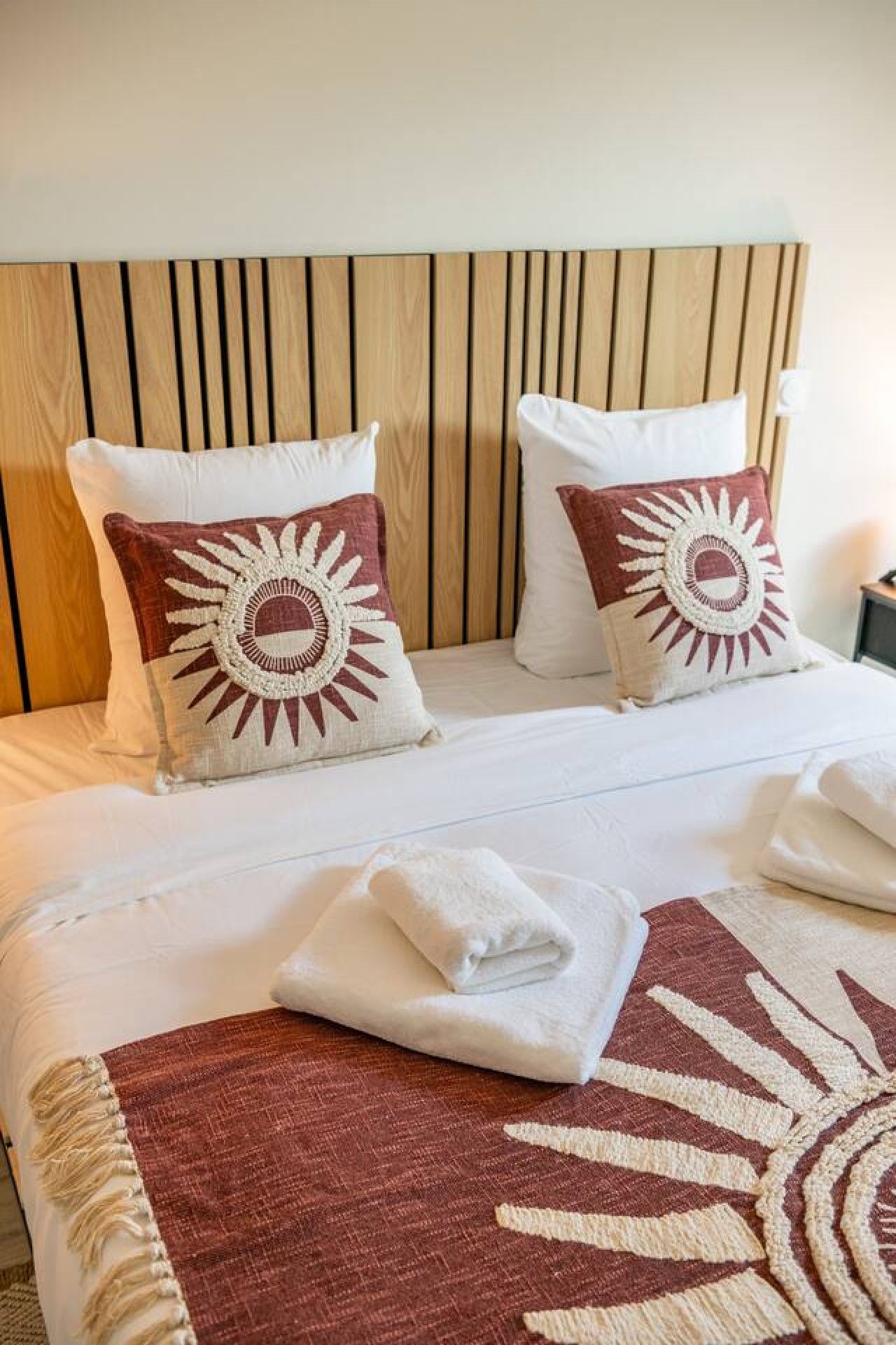 A bed with two pillows, a wooden headboard, and a folded towel on the bed.