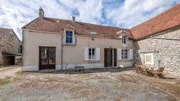 A two-story house with a gravel courtyard, wooden shutters, and a stone wall.