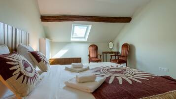 A bedroom with a bed, two chairs, a small table, a mirror, and a skylight.