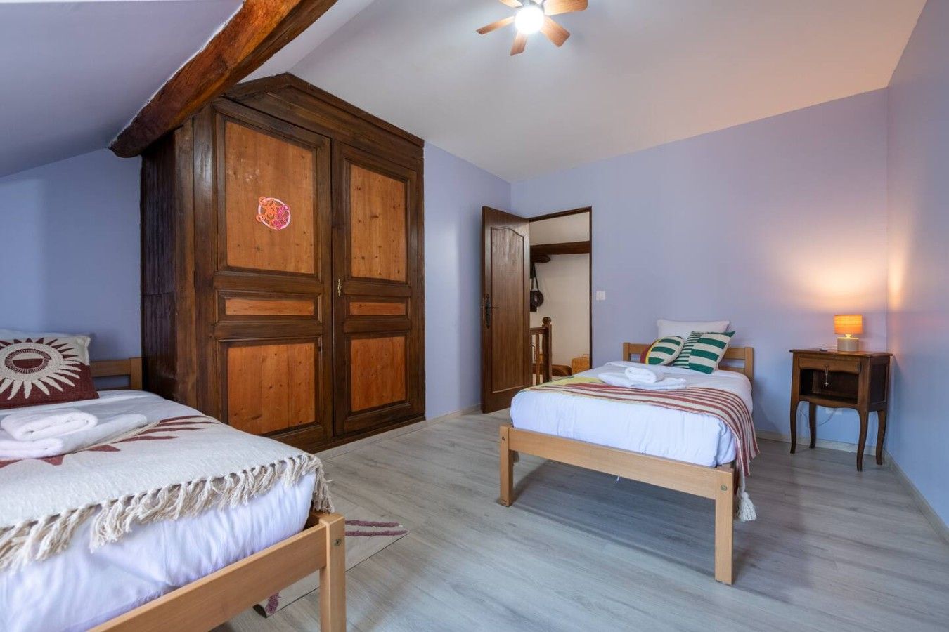 A bedroom with two beds, wooden wardrobe, and a ceiling fan.