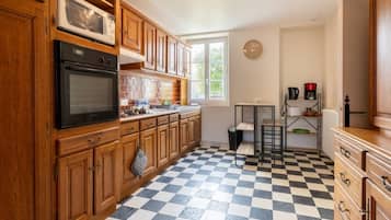 Una cocina con armarios de madera, un horno negro, un microondas, piso a cuadros y una ventana con vista a follaje.