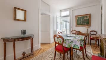 Un coin repas avec une table dressée pour quatre personnes, des chaises en bois, une petite table d’appoint et un tableau accroché au mur.