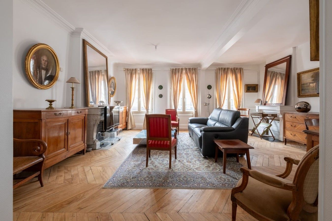 A spacious living room with a fireplace, leather sofa, and a red armchair.