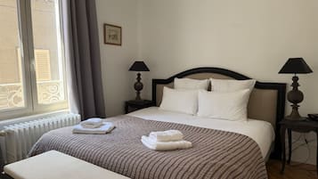 A hotel room with a bed, two bedside tables, a window with curtains, and a radiator.