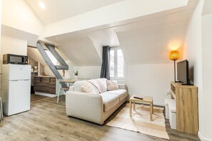 Un loft moderno con cocina, sala de estar con sofá y televisor, y una escalera que lleva a un nivel superior.