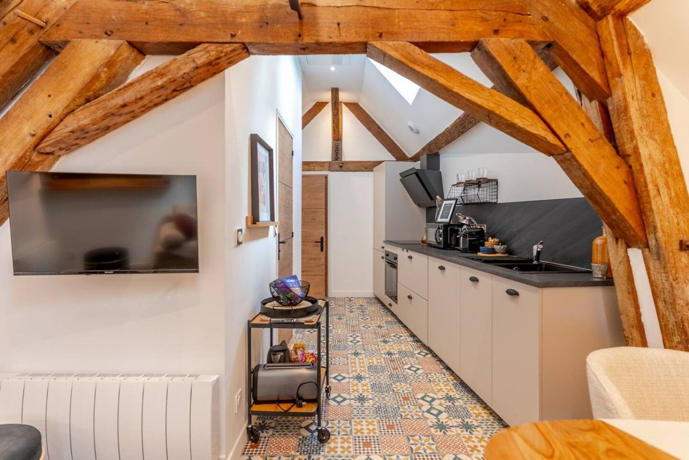 Un petit espace mansardé comprenant un coin cuisine, un téléviseur fixé au mur et un sol à motifs.