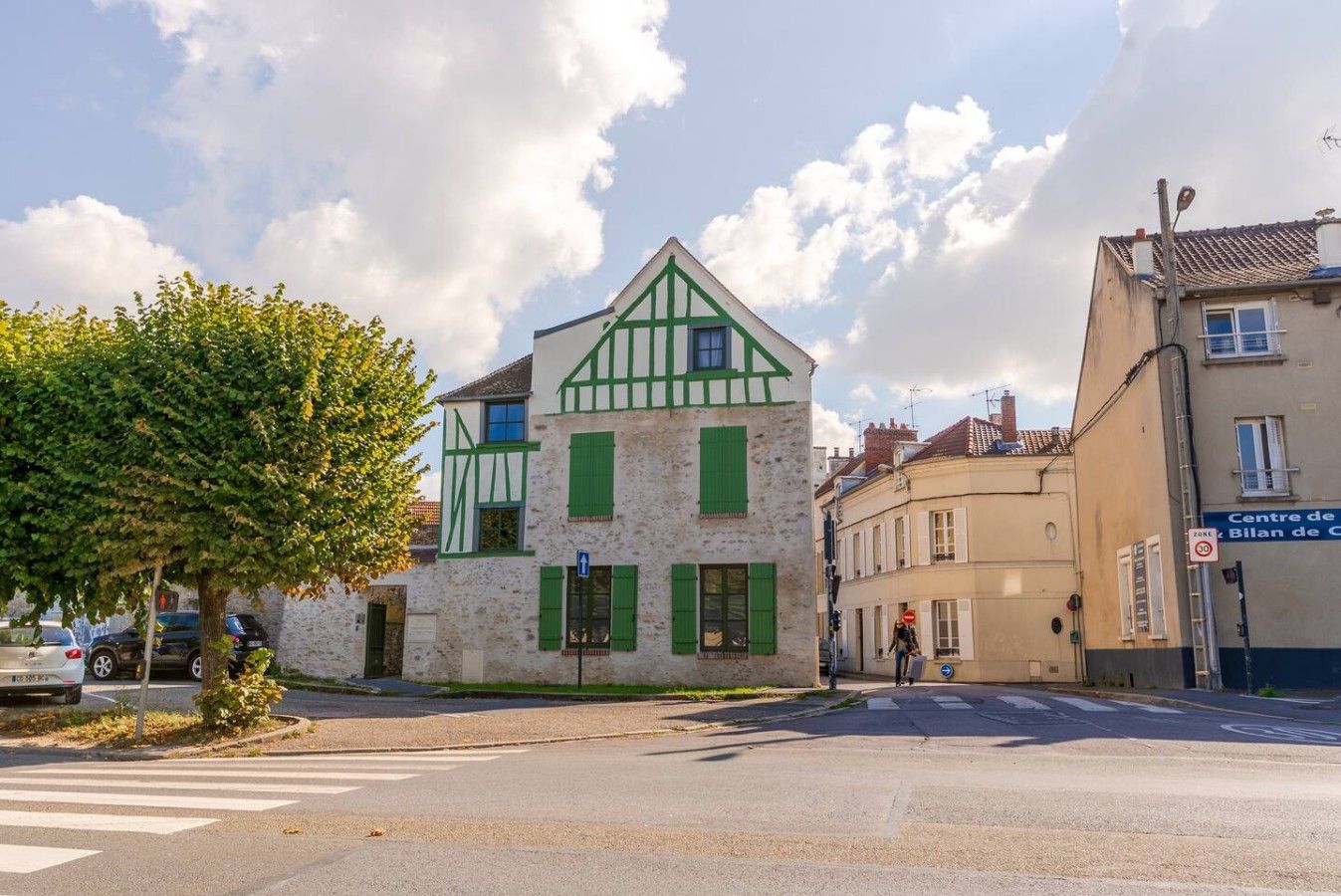 A street view with a building featuring a traditional facade with green shutters and a white and green timber frame.