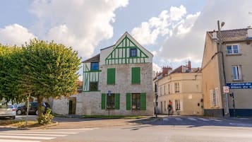 A street view with a building featuring a traditional facade with green shutters and a white and green timber frame.