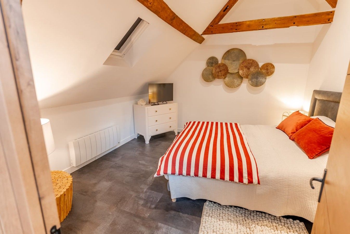 A bedroom with a sloped ceiling, a bed with red and white striped bedding, a white dresser, and a wall-mounted decorative item.