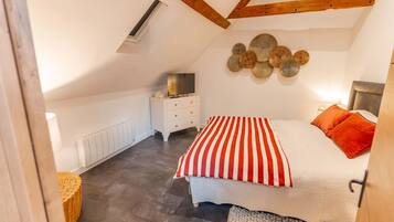 A bedroom with a sloped ceiling, a bed with red and white striped bedding, a white dresser, and a wall-mounted decorative item.