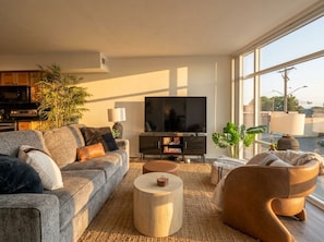 Ein modernes Wohnzimmer mit einer Couch, einem Couchtisch und einem Sessel, einem Flachbildfernseher und einem großen Fenster mit Blick nach außen.