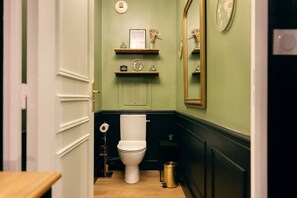 Une salle de bain comprenant des toilettes, un lavabo, un miroir et une étagère avec des objets décoratifs.