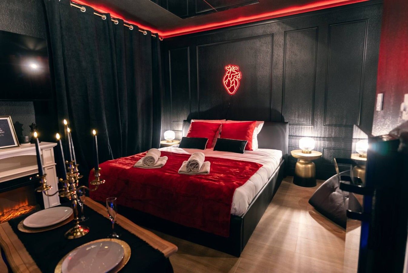 A modern bedroom with a large bed, red bedding, and a neon heart decoration on the wall.