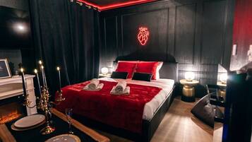 A modern bedroom with a large bed, red bedding, and a neon heart decoration on the wall.