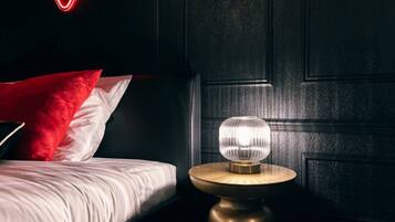 A bedroom with a bed, a round nightstand with a lamp, and a neon heart sign on the wall.