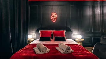Une chambre d’hôtel avec un grand lit, une literie rouge, un cœur lumineux accroché au mur et deux lampes de chevet.