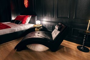 A modern bedroom with a bed, a bedside table with a lamp, and a leather chair.