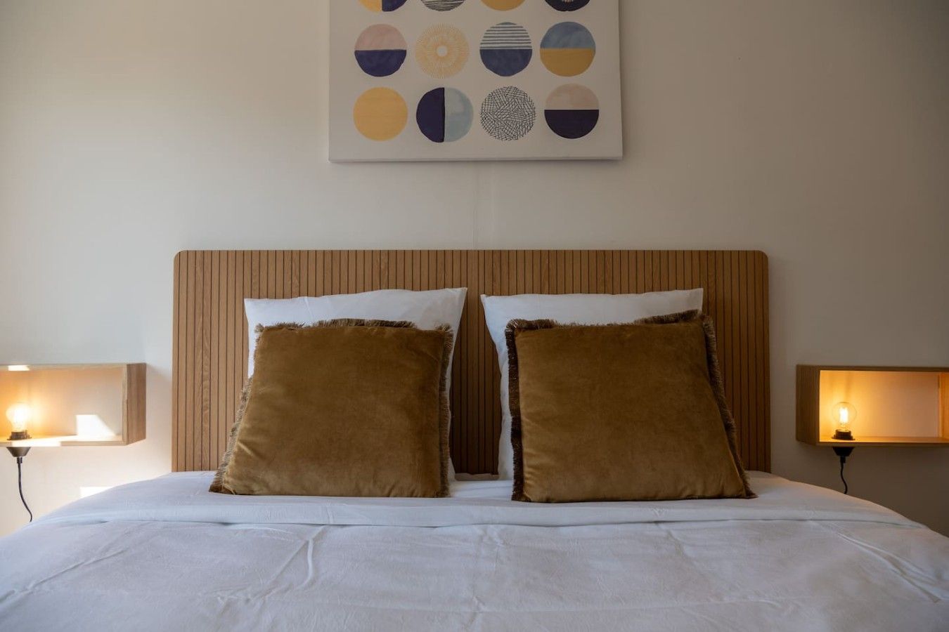 A hotel room with a large bed, two pillows, a headboard, and a wall art piece above the bed.