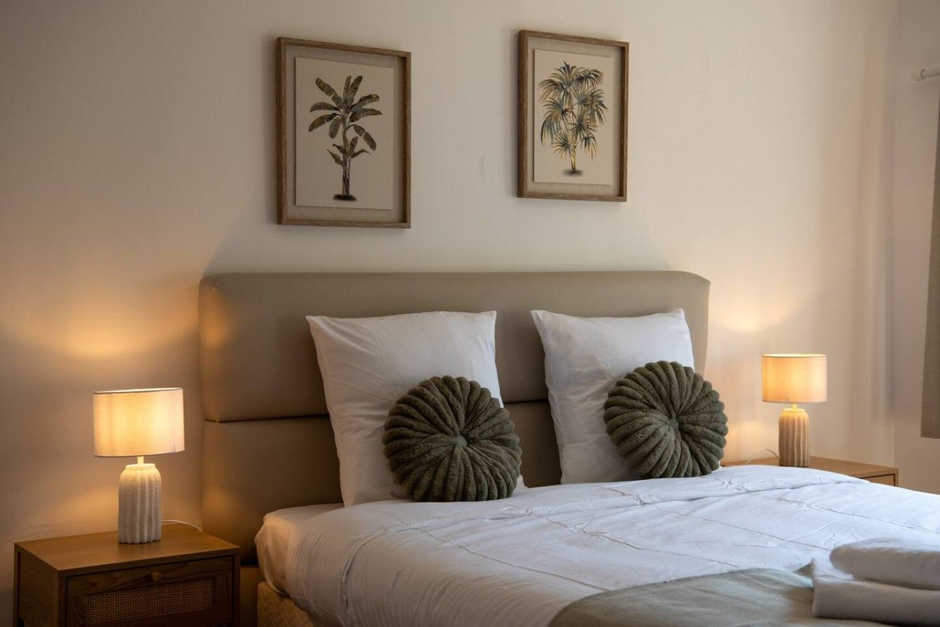 Ein Hotelzimmer mit einem Bett, zwei Nachttischlampen, einem Kopfteil und zwei gerahmten Pflanzenbildern an der Wand.