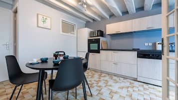 A modern kitchen with a dining area, featuring a herringbone floor pattern, light-colored cabinetry, and black chairs.