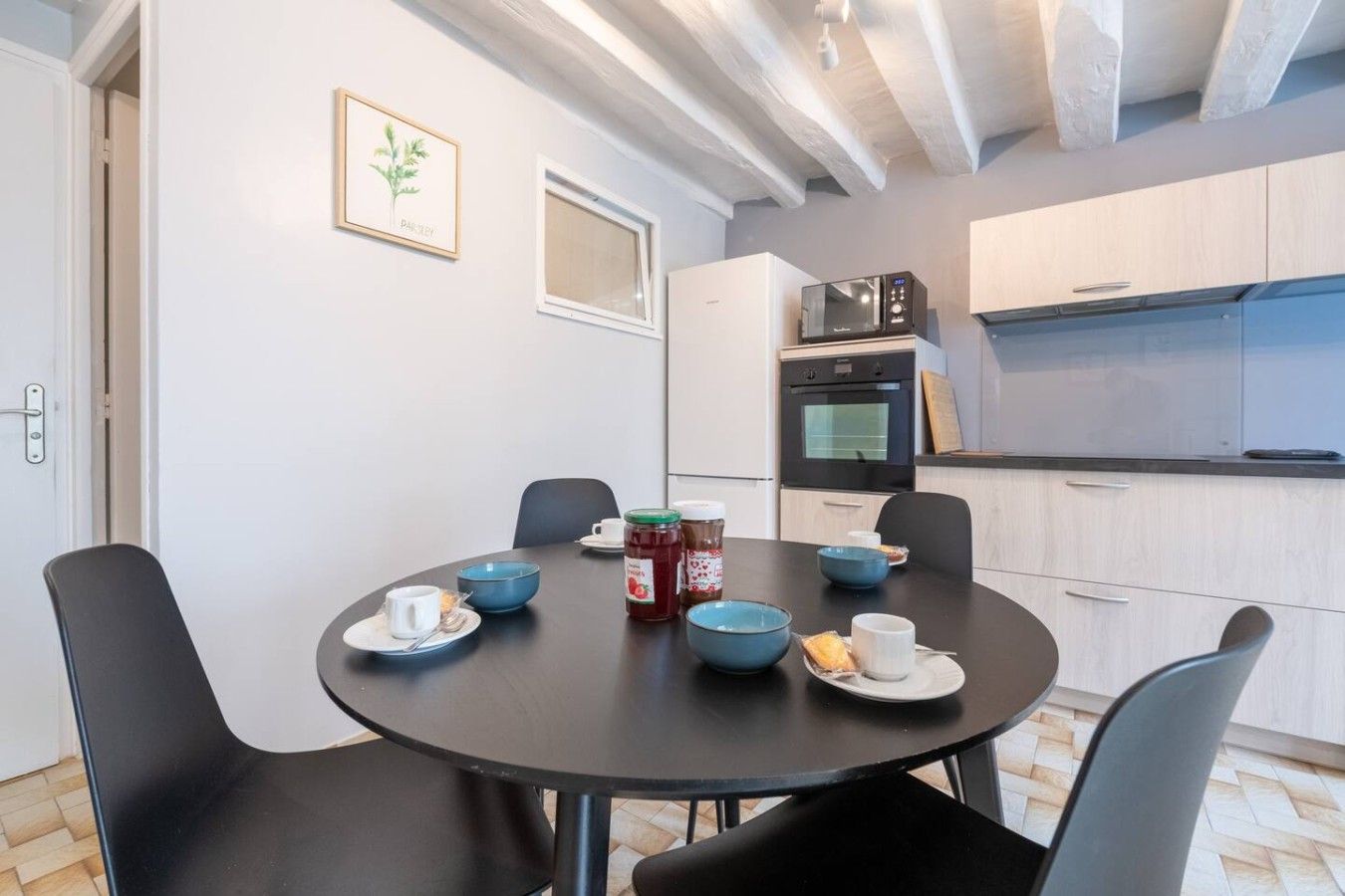 Una cocina moderna con armarios blancos, un microondas negro y un comedor con una mesa redonda y sillas.