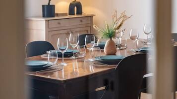Un coin repas avec une table dressée pour quatre personnes, des chaises, une plante en pot et une lampe.