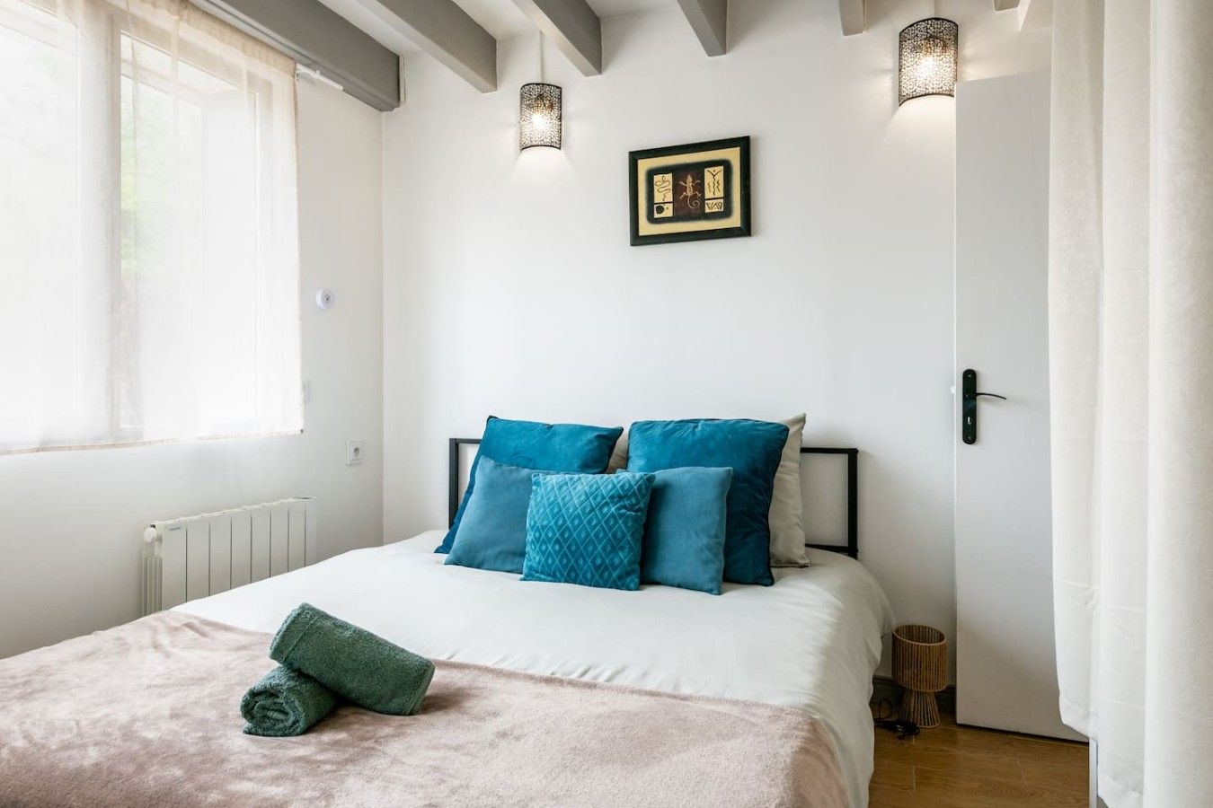 Une chambre à coucher avec un lit, des oreillers, une table de chevet, une lampe et un tableau encadré au mur.