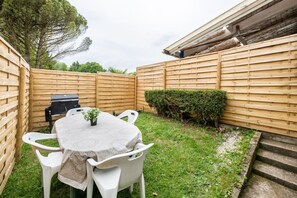 A backyard with a round table, white chairs, a barbecue grill, and a wooden fence. - Le Clos des Chevaux - Stylish Duplex with Garden (La Celle-sur-Morin)