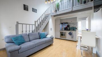 Ein modernes Wohnzimmer mit einem grauen Sofa, einer Treppe, einer Küche und einem Essbereich.