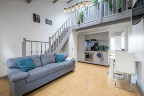 A modern living room with a grey sofa, a staircase, a kitchen, and a dining area. - Le Clos des Chevaux - Stylish Duplex with Garden (La Celle-sur-Morin)