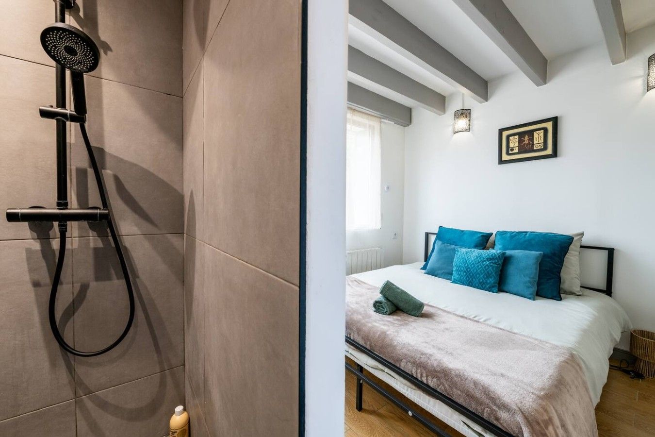 A bathroom with a shower and a bed with blue pillows.