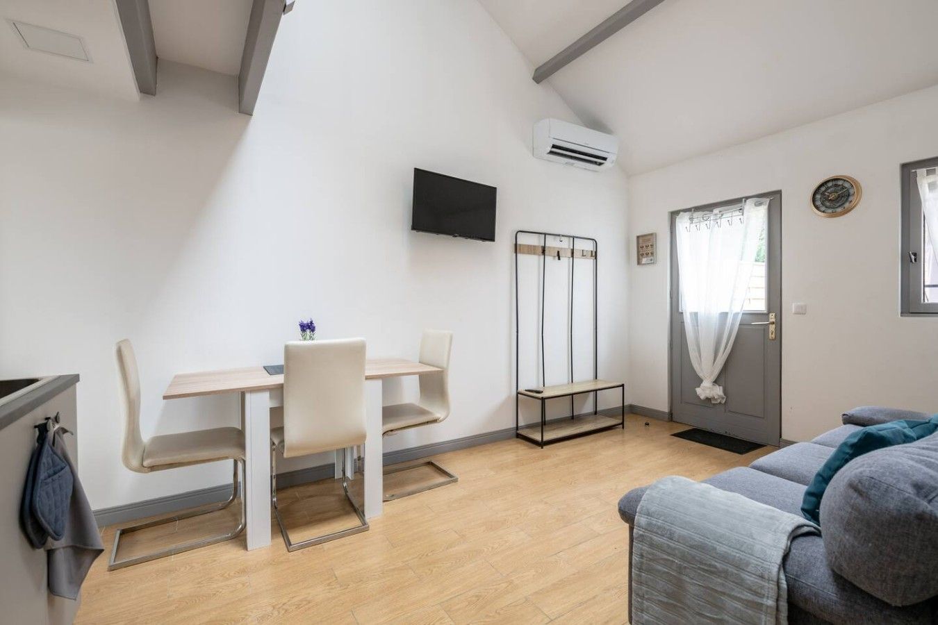 Un espai habitable compacte amb zona de menjador, un sofà, un televisor penjat a la paret i una porta amb cortina.