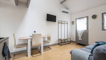 Un espai habitable compacte amb zona de menjador, un sofà, un televisor penjat a la paret i una porta amb cortina.