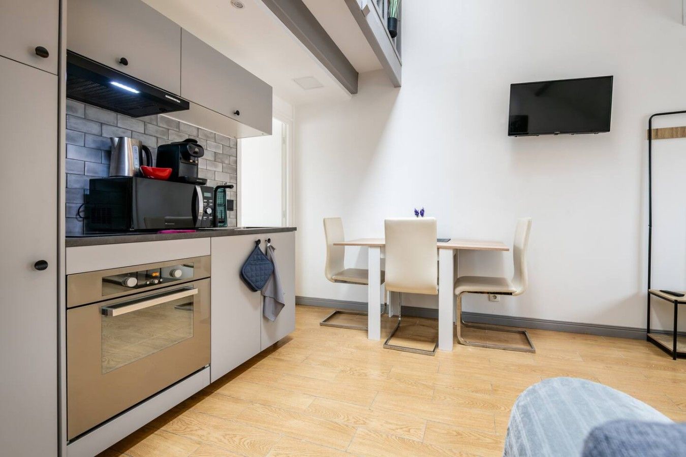 A compact kitchen with modern appliances, a dining area with a table and chairs, and a flat-screen TV mounted on the wall.