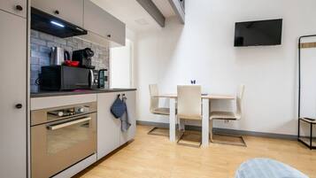 A compact kitchen with modern appliances, a dining area with a table and chairs, and a flat-screen TV mounted on the wall.