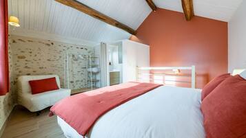 A bedroom with a bed, a white chair, a wardrobe, and a glass shower enclosure.