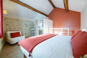 A bedroom with a bed, a white chair, a wardrobe, and a glass shower enclosure. - La Blandynette—renovated and charming (Blandy)